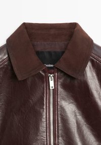 Giacca in pelle bordeaux con colletto in camoscio marrone scuro, dotata di cerniera argentata e dettagli cuciti sulle spalle.