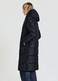 Manteau matelassé noir avec capuche, poches latérales et boutons décoratifs. Présente un design matelassé avec une silhouette longue et une texture lisse.