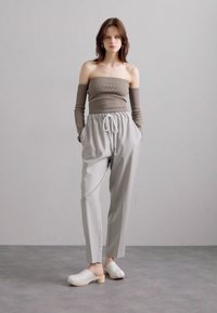 Beige ribbet off-shoulder topp, lysegrå elastisk midje bukser med lommer, og hvite tresko med tre såler. Jevne teksturer generelt.