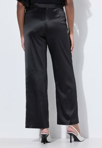 Černé saténové kalhoty s širokými nohavicemi a elastickým pasem, hladká textura a modelka v stříbrných lodičkách na vysokém podpatku.