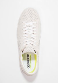 Ljusbeige sneakers med perforerad mockaöverdela, vita snören och vit gummisula. Har en neonorange innersula med "Converse med Lunarlon"-logotyp.
