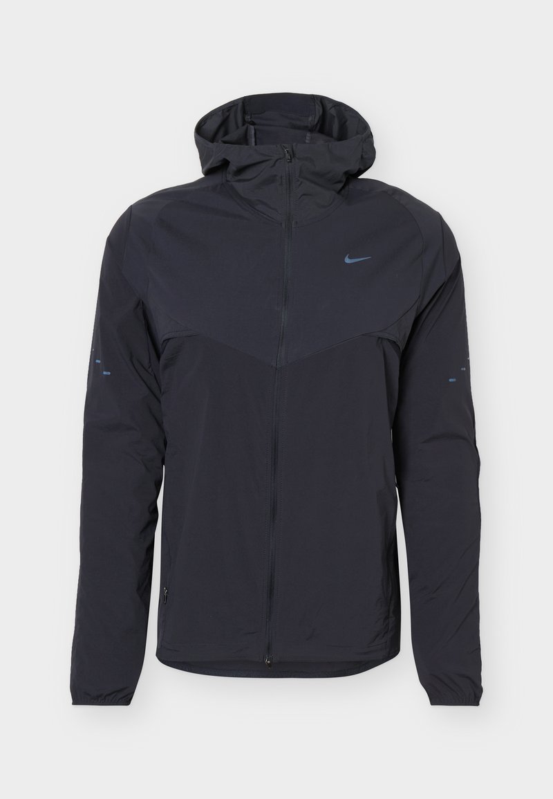 Chaqueta negra ligera con capucha, cremallera completa frontal, puños elásticos y pequeño logotipo Nike Swoosh en el pecho y las mangas.