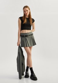 Falda pantalón gris con un cinturón negro, combinada con un top corto negro y zapatos de plataforma negros. Modelo sosteniendo un blazer gris.