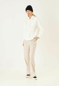 Chemise blanche à boutons avec deux poches poitrine, assortie à un pantalon large beige clair. Un bonnet noir et des chaussures avec des accents noirs complètent le look.