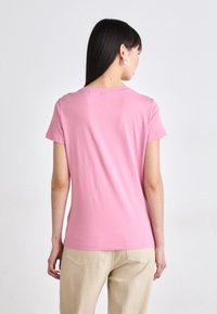 Pink cotton t-shirt with short sleeves and a round neckline. Smooth texture, fitted shape. Worn with beige pants, showing a casual style.