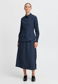 Lungo vestito navy con sottili righe verticali, stile camicia con bottoni, spacchi laterali e scarpe nere; tessuto liscio con un design classico.