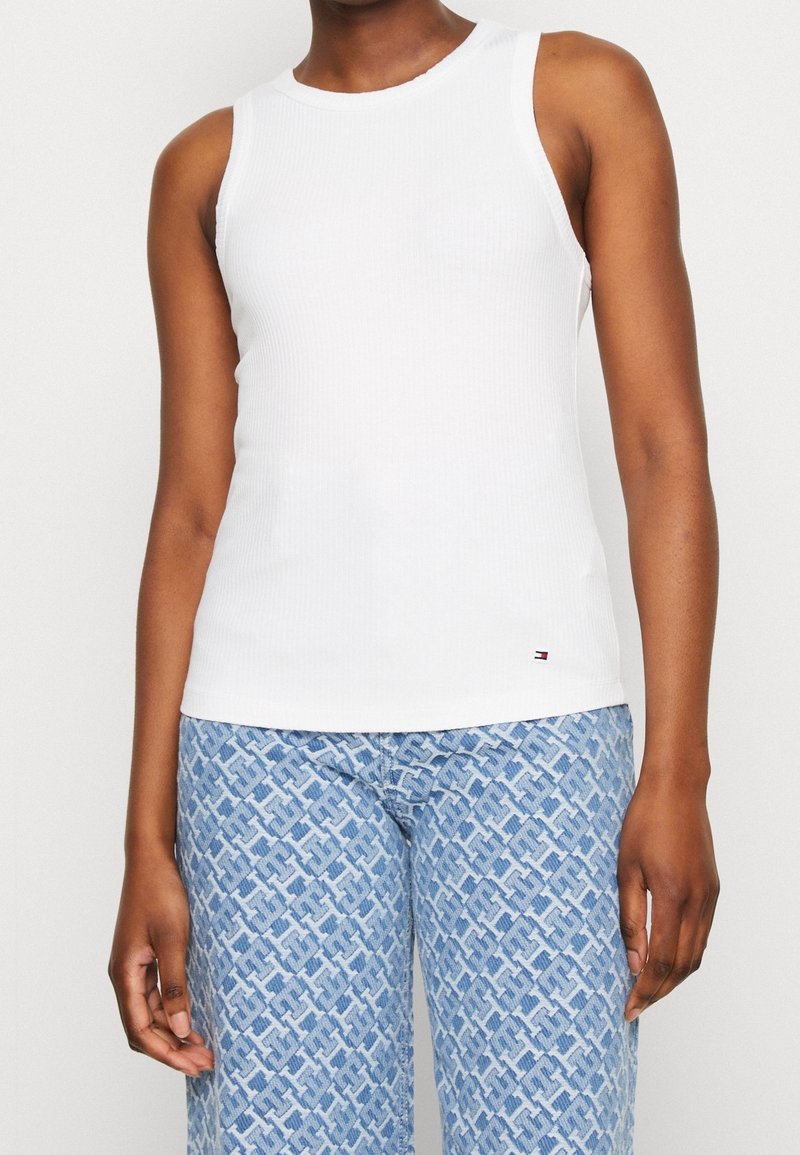 Top bianco a coste senza maniche con scollo tondo, design aderente e piccolo logo sulla piega, abbinato a pantaloni larghi blu con motivo a fantasia.