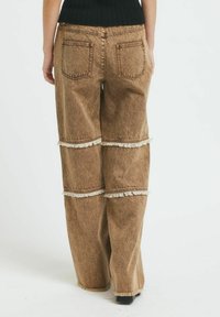 Rjave denim hlače širokega kroja z raztrganimi vodoravnimi šivi. Imajo dva zadnja žepa in teksturirano tkanino. Ohlapen fit, dolga dolžina.