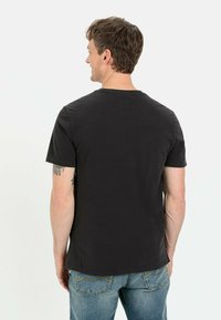 Schwarzes Kurzarm-T-Shirt aus strukturiertem Stoff, mit Rundhalsausschnitt und entspannter Passform, kombiniert mit hellblauen Jeans.