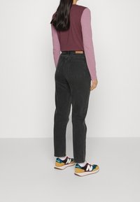 Top s dlouhým rukávem v barvách burgundské a světle růžové, v kombinaci s černými džínami. Barevné sportovní boty s vzorovanými doplňky.