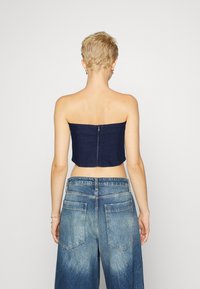 Denim cropped bandeau top so skrytým zipsom na chrbte. Modelka ho kombinuje s svetlomodrými širokými džínami s vreckami na zadnej strane.