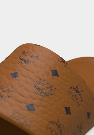 Brun teksturert lærstropp til sandaler med gjentatte svarte MCM-logoer og diamantformede mønstre.