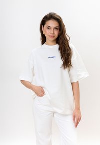 Witte oversized T-shirt met korte mouwen en een ronde halslijn, met de tekst "MIRONS" in het blauw gedrukt op de borst. Zachte katoenen stof.