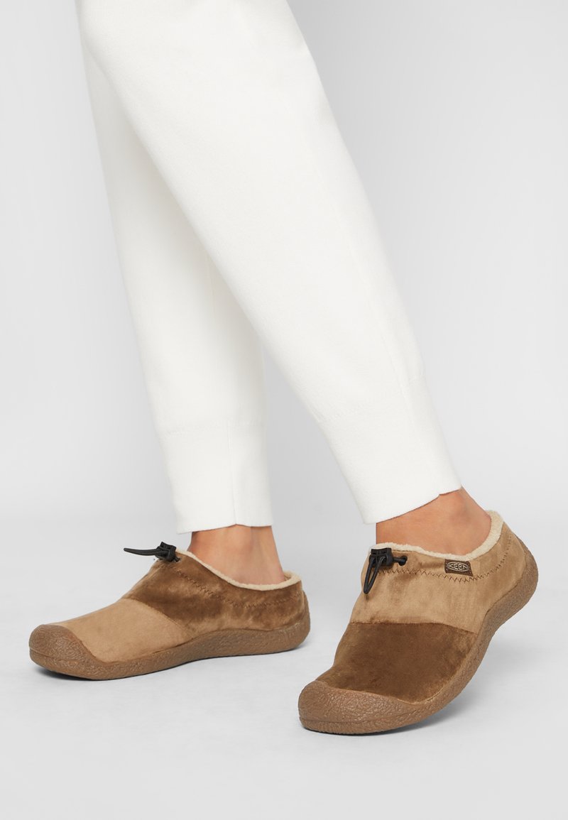 Braune Slipper aus Wildleder und Synthetikobermaterial, mit einer strukturierten Gummisohle, verstellbarem Schnürsenkel und einem flauschigen Rand.