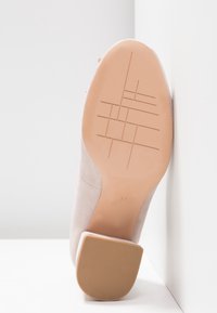 Chaussure en daim beige reposant sur le talon, montrant une semelle lisse avec un motif géométrique de bande de roulement et un tampon de taille 37.