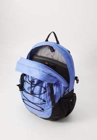 Kék nylon hátizsák, nagy nyitott rekesszel, állítható pántokkal, hálós oldalsó zsebbel és elasztikus bungee zsinór dizájnnal elöl.