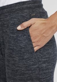 Hallid, tekstuuriga hallid spordipüksid, millel on tihe vöökoht ja küljetasku, ning väike metallist logo silt. Pinnal on pehme, kudumise välimus.