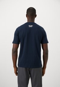 T-shirt de algodão azul marinho com mangas curtas, decote redondo e um logótipo refletor na parte superior das costas. Textura suave e design ajustado.