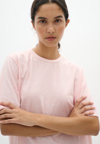 Šviesiai rožinė, trumpa rankovė marškinėliai turi laisvą siluetą ir minkštą tekstūrą, su subtiliu švelniu raštu ir apvaliu iškirpimu.