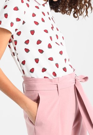 Top blanco de manga corta con estampado de fresas rojas, combinado con pantalones rosa de talle alto con cinturón atado y bolsillos laterales.