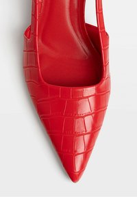 Chaussure rouge à bout pointu avec un motif crocodile brillant et une découpe ouverte sur le côté intérieur sur fond blanc.