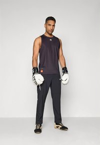 Sort ærmeløs sportslig skjorte, sorte bukser og hvide boksehandsker. Skjorten har et logo, og bukserne har en tekstureret finish.