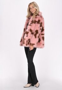 Faux fur-kappa i rosa med bruna abstrakta mönster, med en knappstängning och en avslappnad passform. Buren över svarta utsvängda jeans och beige klackar.
