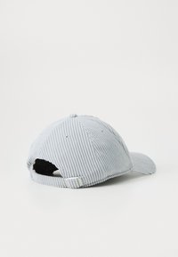 Gorra de béisbol de corduroy gris claro vista desde atrás, mostrando el tejido texturizado y una correa ajustable en la parte trasera.