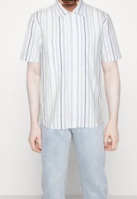 Camicia a maniche corte con strisce verticali blu e bianche, design con bottoni sul davanti, due tasche sul petto e una vestibilità rilassata.