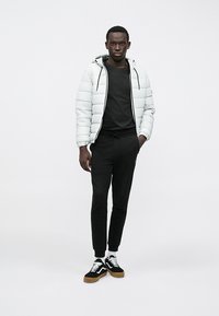 Λευκή μπουφάν με κουκούλα, μαύρη μπλούζα, μαύρο παντελόνι φόρμας και μαύρα αθλητικά με λευκές λεπτομέρειες και καφετιά σόλα. Απλός σχεδιασμός και εφαρμογή.