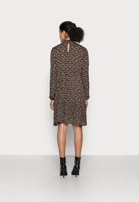 Abito nero floreale con maniche lunghe, scollo arricciato, retro con apertura a chiave e orlo svasato. La modella indossa stivali neri con tacco.