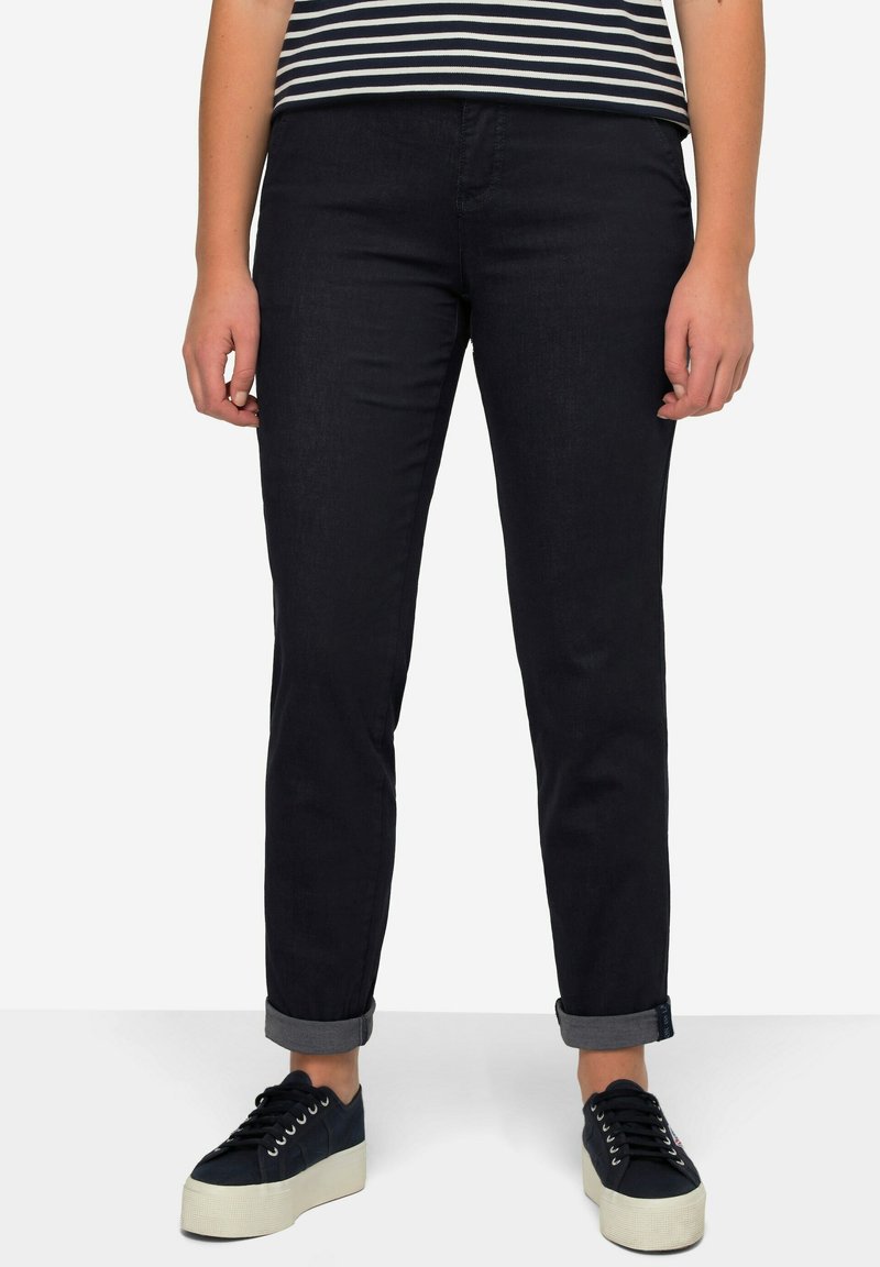 Jeans in denim scuro con una vestibilità dritta, risvolti alle caviglie e dettagli di cucitura sottili, abbinati a una maglietta a righe a maniche corte e sneakers con platform.