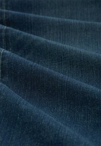 Tela de mezclilla de color azul oscuro con una textura suave y un diseño de sarga distintivo, con sutiles desvanecimientos y detalles de costura.