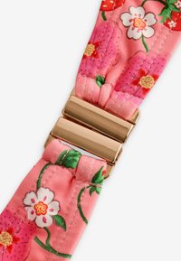 Cvečni pašček za uro v roza tkanini z belimi in rdečimi cvetovi, z bleščečo zlatotonečno kovinsko zaponko za varno zapiranje.