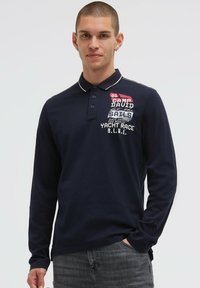 Marineblaues Langarm-Poloshirt mit weißem Kragen und Bündchen, vorne mit farbenfroher Grafik und Schriftzug. Weiche, glatte Stofftextur.