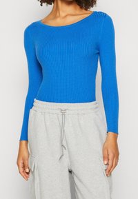 Ribbed blue long-sleeve top with a wide neckline, paired with gray sweatpants featuring side pockets and an elastic waistband.