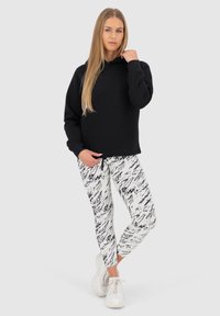 Felpa nera con vestibilità comoda e maniche lunghe, abbinata a leggings bianchi con un motivo astratto nero e scarpe da ginnastica bianche.