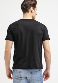 Camiseta de algodón negra de manga corta, con un cuello redondo y un corte recto, combinada con jeans de mezclilla azul claro. Textura suave, sin patrones.