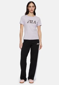 Camiseta de color púrpura claro con el logo de FILA, combinada con joggers negros que cuentan con una raya blanca lateral y la marca FILA en la parte frontal.