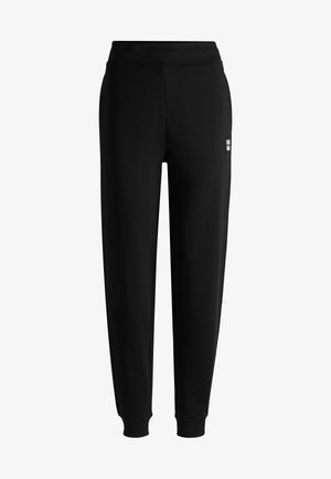 Pantaloni della tuta neri con una vita a coste, gambe affusolate e un piccolo logo bianco sul retro. Realizzati in un materiale morbido e liscio.