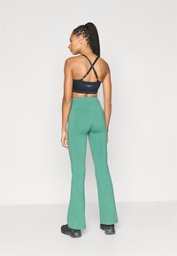 Μαύρο αθλητικό μπουστάκι με λουριά που σταυρώνουν στην πλάτη και λογότυπο, σε συνδυασμό με πράσινο καμπανοειδές κολάν. Το ύφασμα φαίνεται λείο με ελαφριά ελαστικότητα.