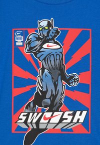 Modrá tričko s grafickým potlačou svalnatej postavy v sivej farbe s akcentmi v zelenej, na pozadí červeného a modrého výbuchu, s textom "SWOOSH".