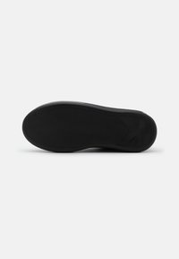 Black rubber shoe sole with textured tread patterns, featuring logo details and a smooth edge. Clean design with no visible markings.