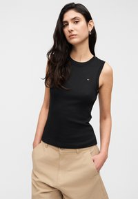 Μαύρο αμάνικο τοπ από βαμβάκι, με στρογγυλή λαιμόκοψη και μικρό, κεντημένο λογότυπο στο στήθος, συνδυασμένο με μπεζ παντελόνια.