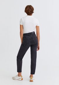 Jean en denim noir taille haute avec poches arrière ; associé à un haut blanc à manches courtes et des baskets blanches avec des accents beige.