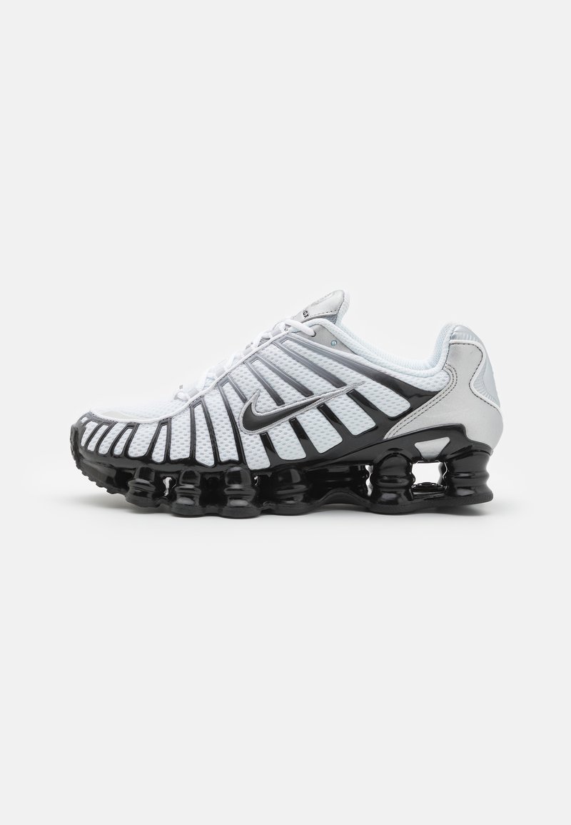 Hvit sportssko med mesh-overdel og svart gummi såle, med en tydelig ribbet design og Nike-logo. Snøring på toppen.