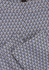 Geweven stof met een geometrisch ontwerp van zwarte en blauwe ruiten op een lichtgrijze achtergrond, met een gladde textuur en fijne stiksels.