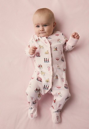 Bebé acostado sobre una manta con rayas rosas, vistiendo un enterizo rosa con estampados temáticos de Londres que incluyen autobuses, guardias, perros y coronas.