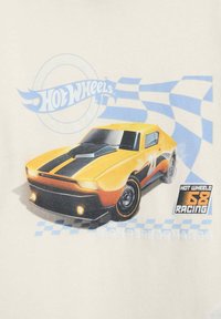 T-shirt Hot Wheels con una macchina sportiva gialla con strisce nere, dettagli grafici e uno sfondo a motivo a scacchi in materiale morbido.
