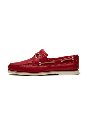 Rotes Leder-Bootsschuh mit beiger Sohle, Mokassinnaht und braunen Leder-Schnürsenkeln, die durch Metallösen an den Seiten und oben gefädelt sind.